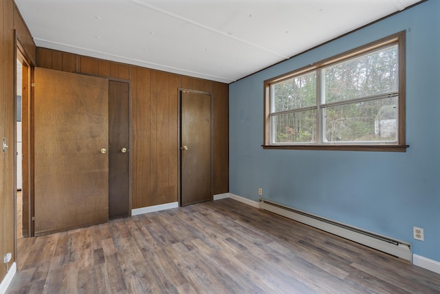 unfurnished bedroom featuring baseboard heating, hardwood / wood-style floors, and wood walls