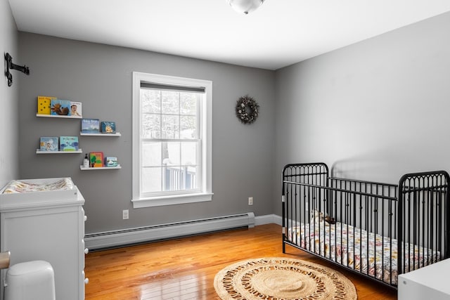 bedroom with a baseboard heating unit, hardwood / wood-style flooring, and a crib