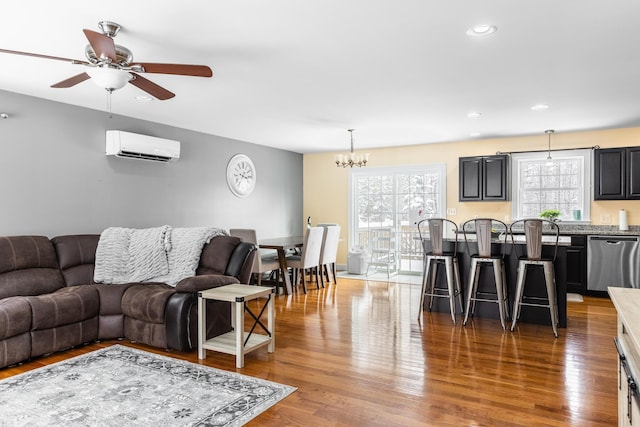 living room featuring hardwood / wood-style floors, ceiling fan with notable chandelier, and a wall mounted AC