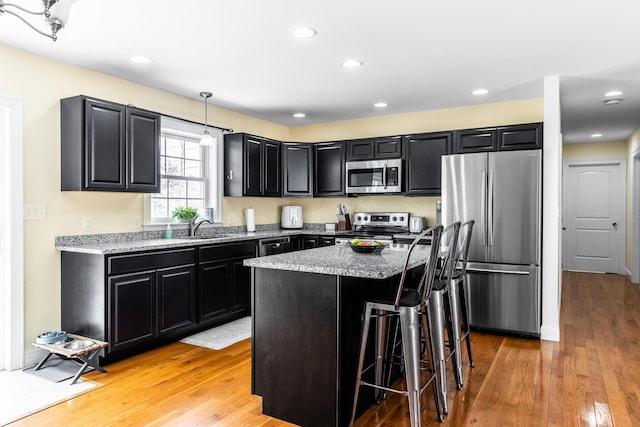 kitchen with a breakfast bar, decorative light fixtures, light wood-type flooring, a kitchen island, and stainless steel appliances