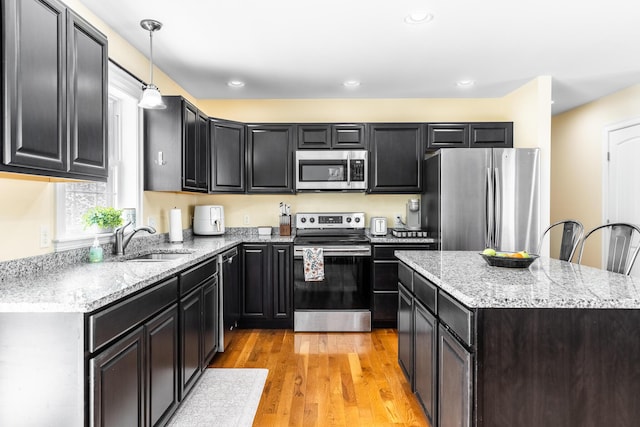 kitchen with appliances with stainless steel finishes, decorative light fixtures, sink, a center island, and light hardwood / wood-style flooring