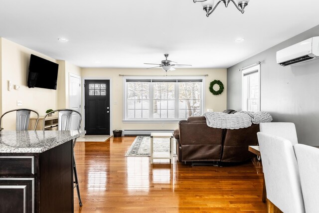 living room with a baseboard heating unit, hardwood / wood-style flooring, a wall unit AC, and ceiling fan