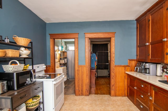 kitchen featuring radiator, wooden walls, light tile patterned flooring, and white electric range oven