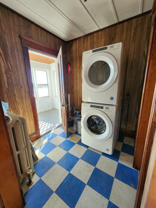 laundry room featuring heating unit, stacked washer and dryer, and wooden walls