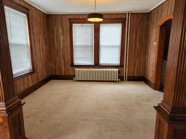 carpeted spare room featuring ornate columns, radiator heating unit, and wood walls