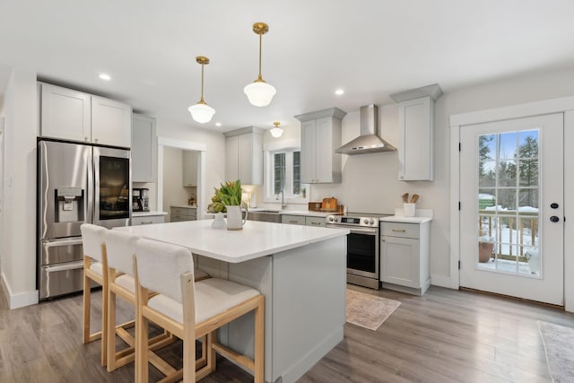 kitchen with wall chimney exhaust hood, a breakfast bar, hanging light fixtures, a kitchen island, and stainless steel appliances