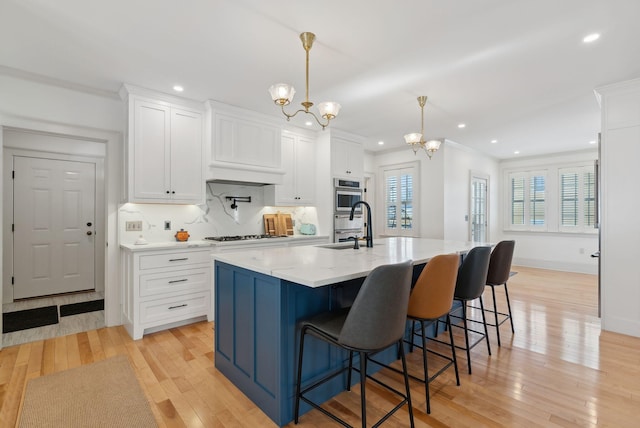 kitchen featuring a kitchen breakfast bar, double oven, an island with sink, pendant lighting, and white cabinets