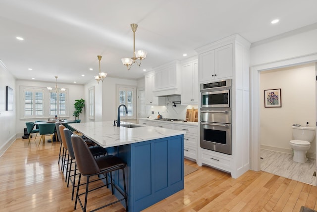 kitchen with pendant lighting, sink, white cabinets, a large island, and a notable chandelier