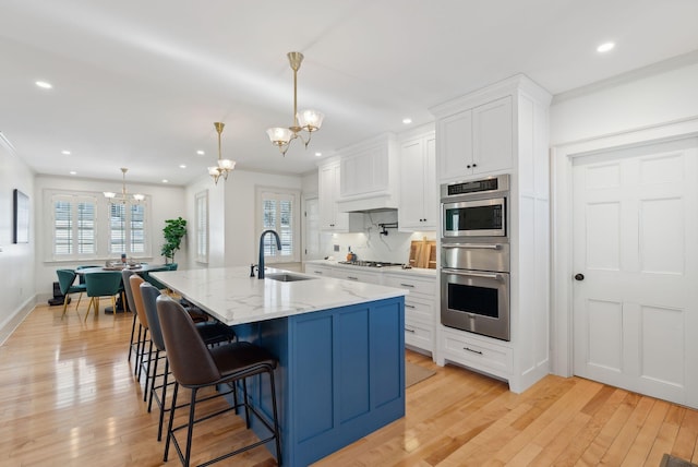 kitchen featuring sink, white cabinetry, a chandelier, a large island with sink, and pendant lighting