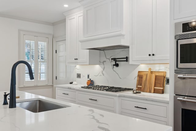 kitchen with sink, ornamental molding, stainless steel appliances, light stone countertops, and white cabinets