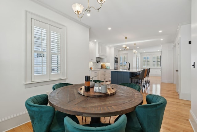 dining space with an inviting chandelier, ornamental molding, sink, and light hardwood / wood-style flooring