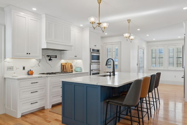 kitchen with decorative light fixtures, an island with sink, sink, white cabinets, and a notable chandelier