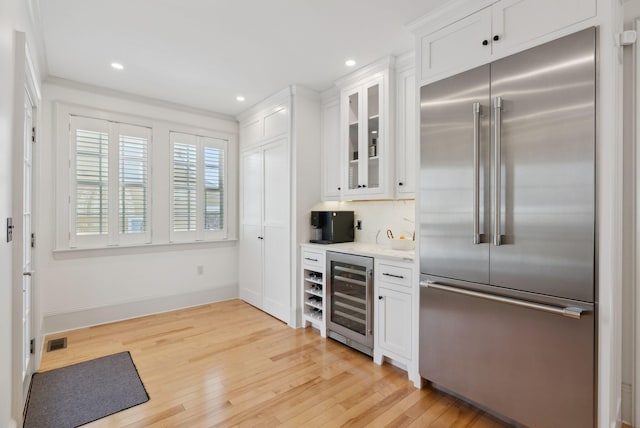 kitchen with white cabinetry, stainless steel built in refrigerator, wine cooler, and light hardwood / wood-style flooring