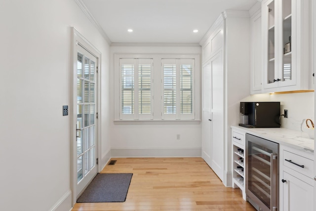 kitchen featuring white cabinetry, crown molding, light hardwood / wood-style flooring, beverage cooler, and light stone countertops