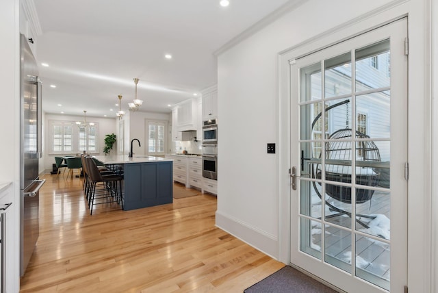 kitchen featuring a breakfast bar, white cabinetry, high end refrigerator, hanging light fixtures, and an island with sink