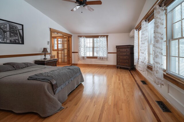 bedroom with a wall mounted air conditioner, lofted ceiling, multiple windows, and light wood-type flooring