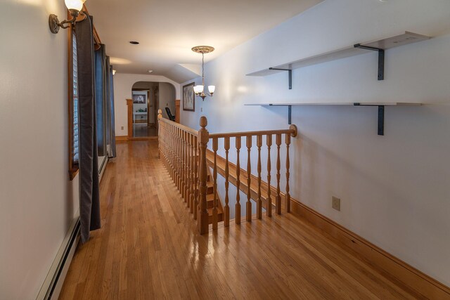 corridor with light hardwood / wood-style floors, a chandelier, and baseboard heating