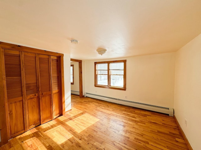 unfurnished bedroom featuring light wood-type flooring, baseboard heating, and a closet