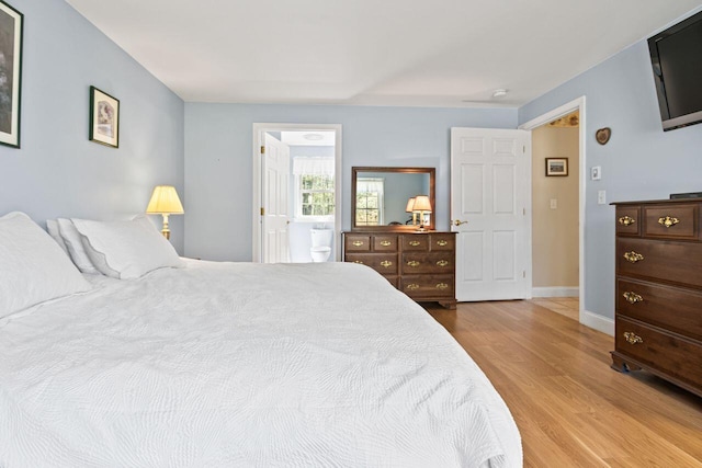 bedroom with baseboards, ensuite bathroom, and wood finished floors