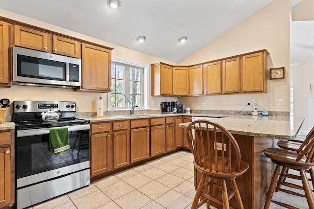 kitchen with a peninsula, lofted ceiling, brown cabinets, and stainless steel appliances