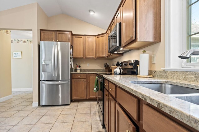 kitchen with lofted ceiling, light tile patterned flooring, brown cabinets, a sink, and stainless steel appliances