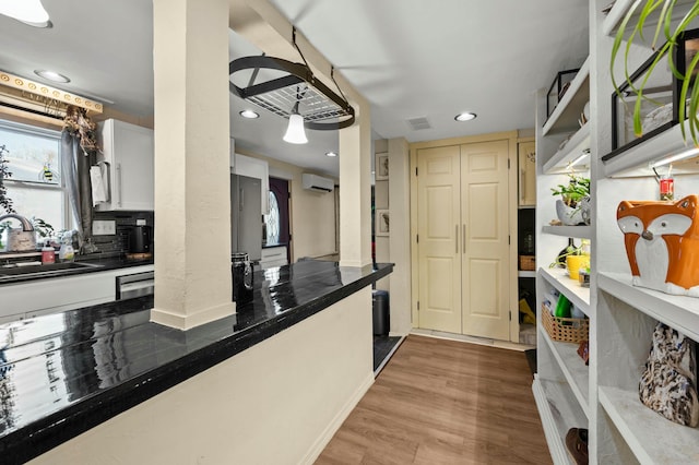 kitchen featuring dark countertops, wood finished floors, a wall mounted air conditioner, open shelves, and a sink