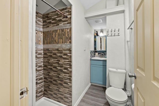 bathroom with visible vents, toilet, wood finished floors, a tile shower, and vanity