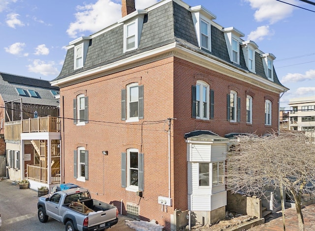 view of home's exterior featuring brick siding, mansard roof, a chimney, and roof with shingles