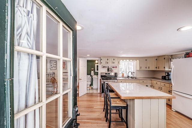 kitchen with tile countertops, sink, white fridge, stainless steel range oven, and light hardwood / wood-style flooring