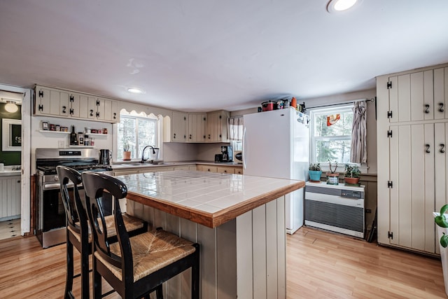 kitchen featuring tile countertops, sink, white refrigerator, stainless steel gas range, and light hardwood / wood-style flooring