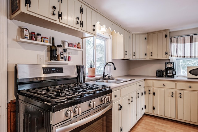 kitchen featuring sink, light hardwood / wood-style floors, stainless steel range with gas stovetop, and white cabinets