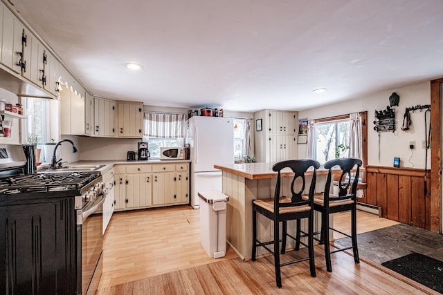 kitchen featuring sink, white appliances, white cabinetry, a kitchen breakfast bar, and light wood-type flooring