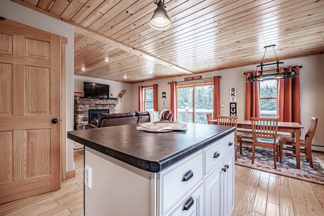 kitchen featuring a stone fireplace, pendant lighting, white cabinetry, a center island, and light hardwood / wood-style flooring