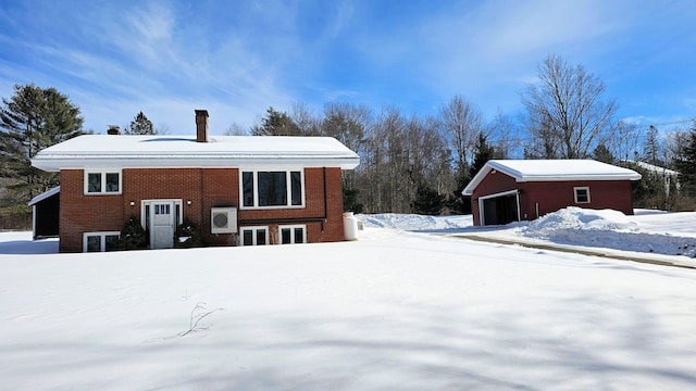 snow covered rear of property with a garage, a chimney, and brick siding