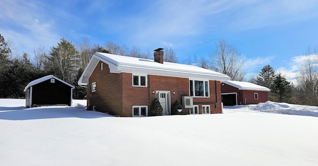 snow covered back of property featuring ac unit, a chimney, a detached garage, and brick siding