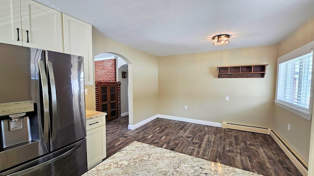 kitchen with arched walkways, dark wood finished floors, white cabinets, light stone countertops, and stainless steel fridge