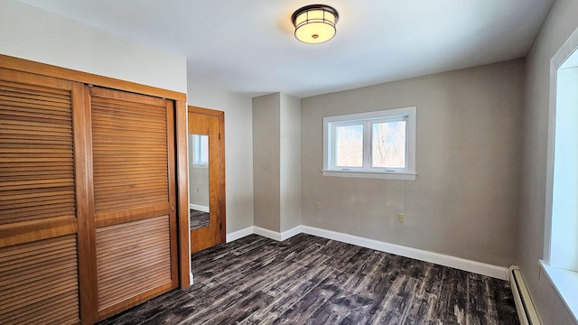 unfurnished bedroom with a baseboard heating unit, a closet, baseboards, and dark wood-style flooring