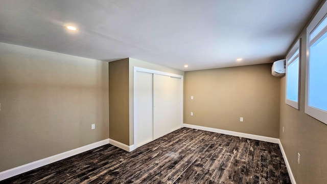 unfurnished bedroom with an AC wall unit, dark wood-style flooring, a closet, and baseboards