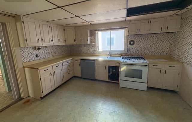 kitchen with white gas range, white cabinets, decorative backsplash, stainless steel dishwasher, and a drop ceiling