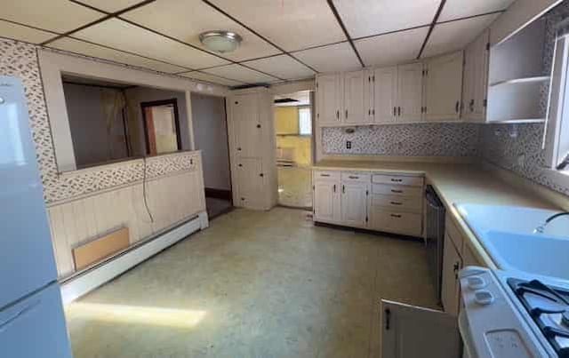 kitchen featuring sink, white appliances, baseboard heating, white cabinets, and a drop ceiling