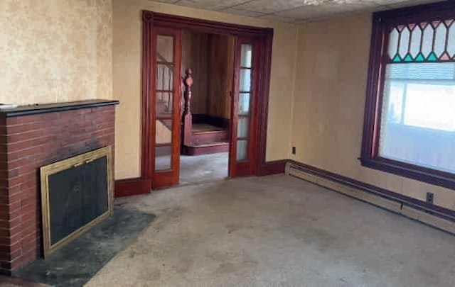 unfurnished living room with carpet floors, a baseboard heating unit, a fireplace, and french doors