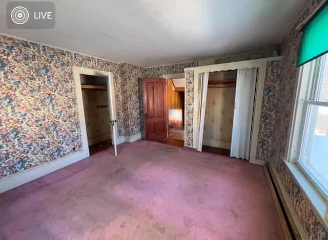 unfurnished bedroom with carpet floors, a baseboard radiator, and multiple closets