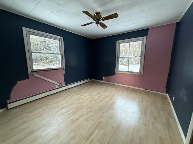 spare room featuring ceiling fan, a baseboard heating unit, and light wood-type flooring