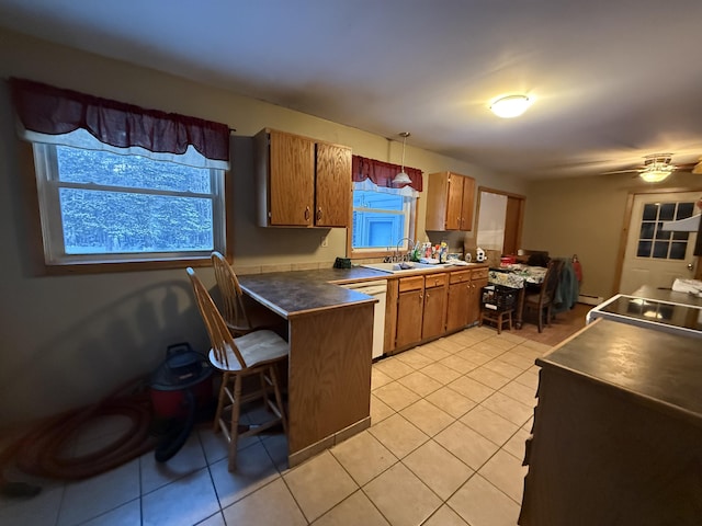 kitchen featuring light tile patterned floors, a breakfast bar, hanging light fixtures, white dishwasher, and kitchen peninsula