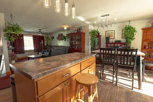 kitchen featuring dark wood-type flooring, dark countertops, open floor plan, and hanging light fixtures