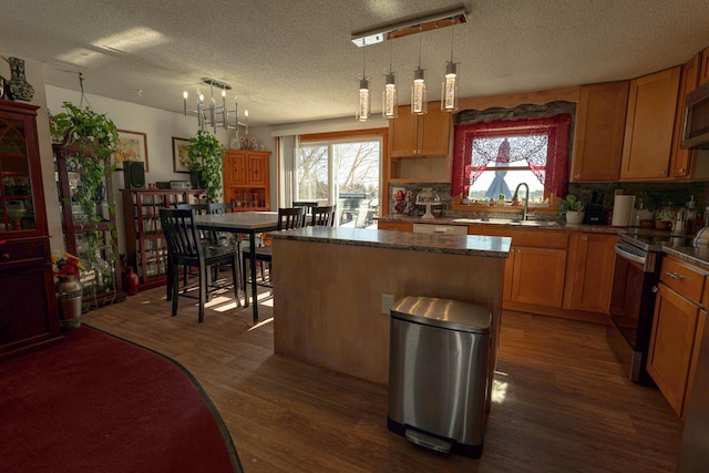 kitchen with dark wood-type flooring, a sink, appliances with stainless steel finishes, a center island, and pendant lighting