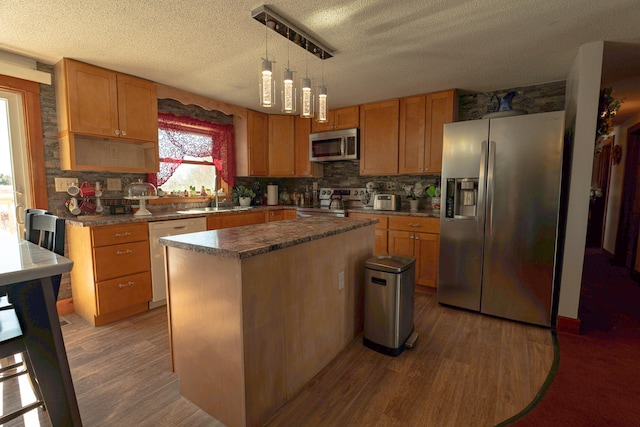 kitchen featuring dark countertops, a kitchen island, appliances with stainless steel finishes, wood finished floors, and hanging light fixtures