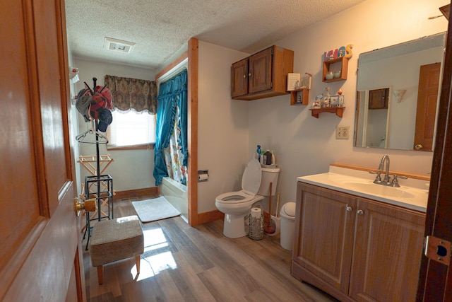 full bathroom featuring a textured ceiling, toilet, wood finished floors, vanity, and shower / bathtub combination with curtain