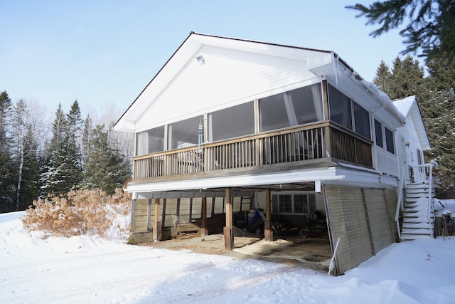 snow covered rear of property with a sunroom