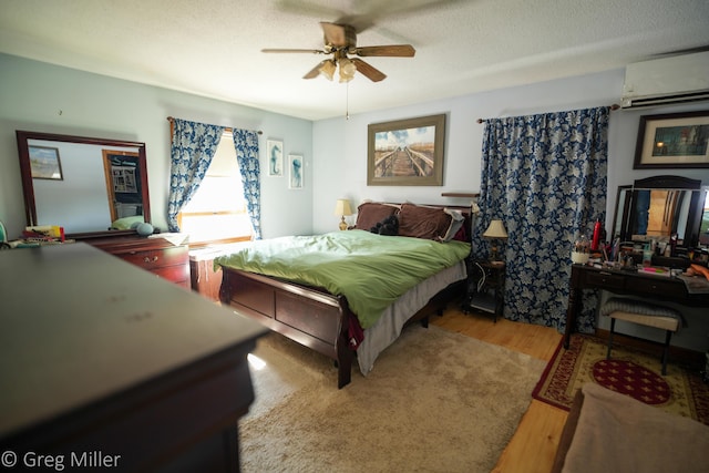 bedroom featuring ceiling fan, a wall mounted air conditioner, a textured ceiling, and light hardwood / wood-style floors